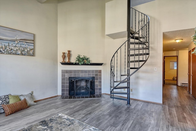 unfurnished living room with a high ceiling, a fireplace, wood finished floors, baseboards, and stairs