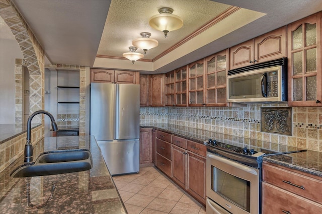 kitchen with a tray ceiling, stainless steel appliances, decorative backsplash, a sink, and a textured ceiling