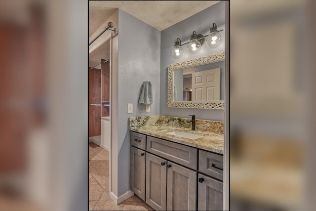 bathroom featuring a textured ceiling, a textured wall, vanity, baseboards, and tile patterned floors