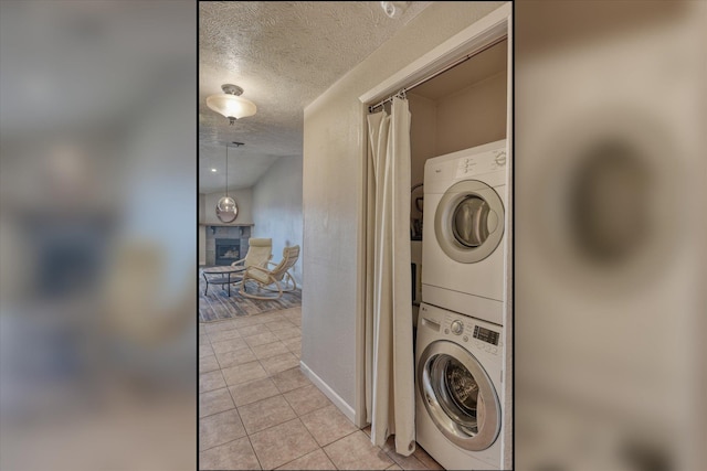 clothes washing area featuring light tile patterned floors, a textured ceiling, laundry area, a fireplace, and stacked washer / drying machine