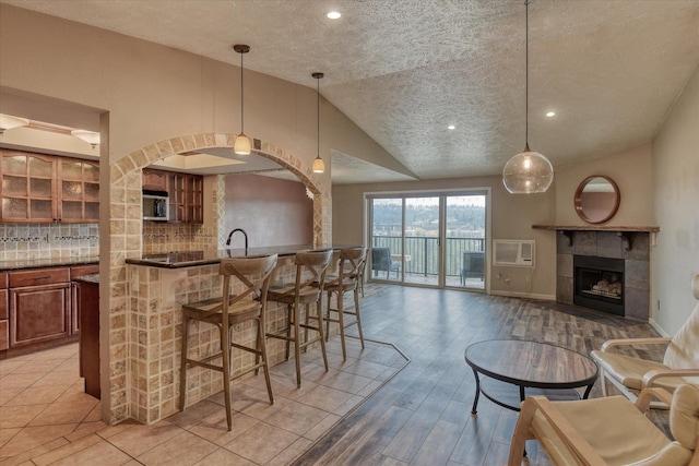 kitchen featuring brown cabinetry, decorative backsplash, a breakfast bar area, stainless steel microwave, and vaulted ceiling