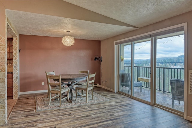 unfurnished dining area featuring an inviting chandelier, a textured ceiling, baseboards, and wood finished floors