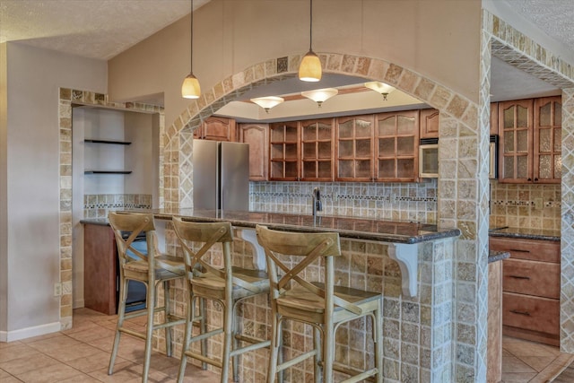 bar featuring tasteful backsplash, decorative light fixtures, a textured ceiling, and freestanding refrigerator