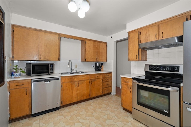 kitchen with under cabinet range hood, a sink, light countertops, appliances with stainless steel finishes, and backsplash