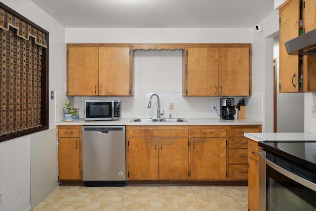 kitchen with stainless steel appliances, a sink, light countertops, decorative backsplash, and brown cabinets