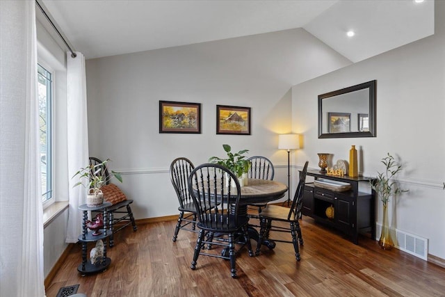 dining room featuring baseboards, visible vents, vaulted ceiling, and wood finished floors