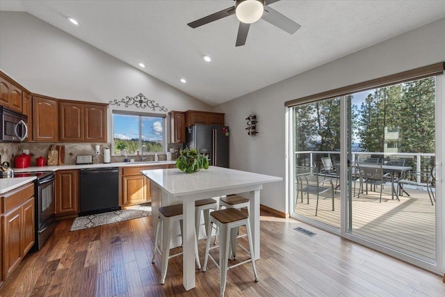 kitchen featuring wood finished floors, a sink, light countertops, black appliances, and a kitchen bar