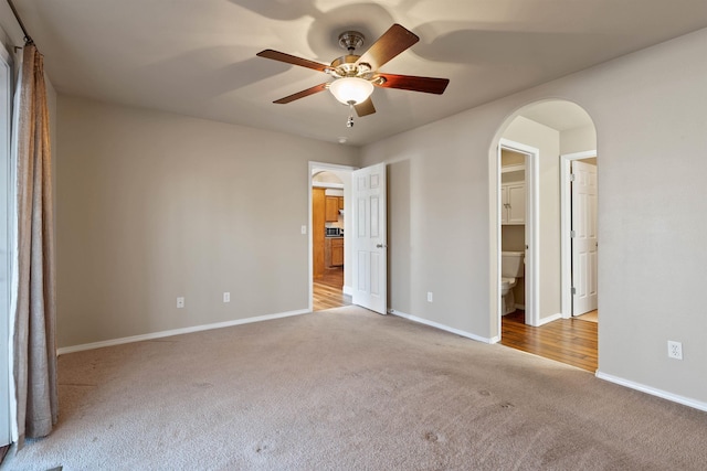 unfurnished bedroom featuring arched walkways, baseboards, a ceiling fan, carpet, and a spacious closet