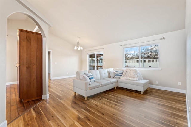 living room with arched walkways, a notable chandelier, light wood finished floors, vaulted ceiling, and baseboards