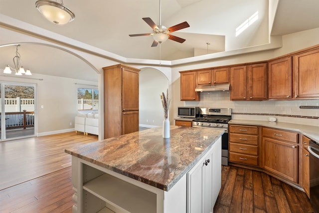 kitchen with arched walkways, under cabinet range hood, vaulted ceiling, appliances with stainless steel finishes, and tasteful backsplash