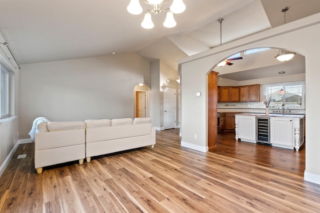 living room with arched walkways, light wood finished floors, lofted ceiling, beverage cooler, and baseboards