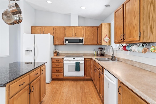 kitchen with light wood finished floors, lofted ceiling, brown cabinetry, a sink, and white appliances