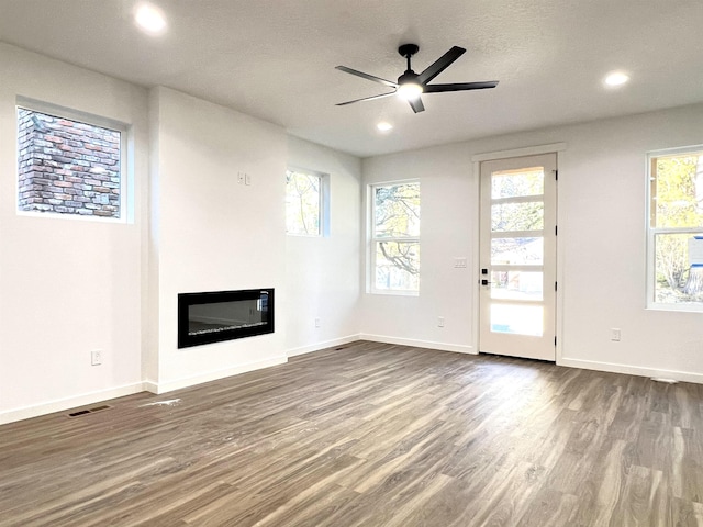 unfurnished living room with dark wood-style floors, a wealth of natural light, a glass covered fireplace, and visible vents