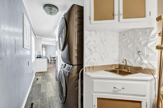 washroom with stacked washer and dryer, a sink, wood finished floors, wet bar, and laundry area