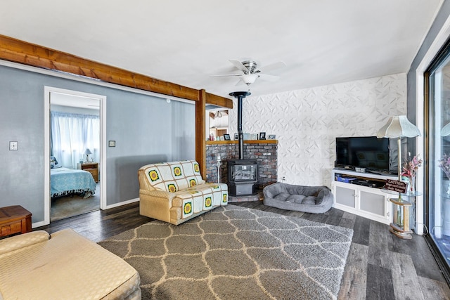 living room featuring a wood stove, ceiling fan, wood finished floors, baseboards, and wallpapered walls