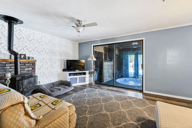 living room featuring a wood stove, ceiling fan, baseboards, and wood finished floors