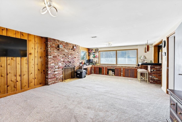 carpeted living area featuring a brick fireplace, wooden walls, and visible vents