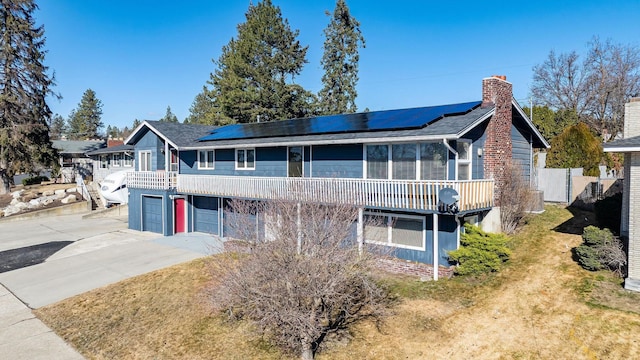 view of front of property with a garage, fence, concrete driveway, roof mounted solar panels, and a chimney