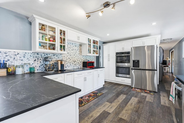 kitchen featuring dark wood finished floors, decorative backsplash, dark countertops, appliances with stainless steel finishes, and white cabinetry