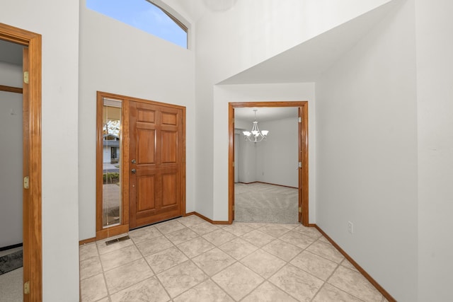 entryway with light tile patterned floors, a notable chandelier, a high ceiling, visible vents, and baseboards