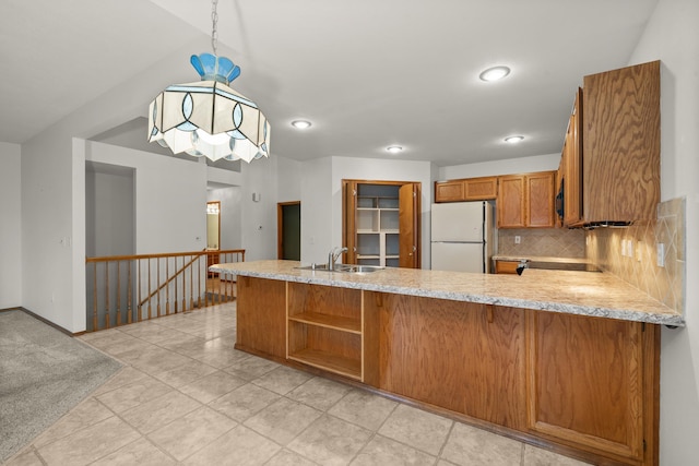 kitchen with brown cabinetry, freestanding refrigerator, a peninsula, a sink, and backsplash