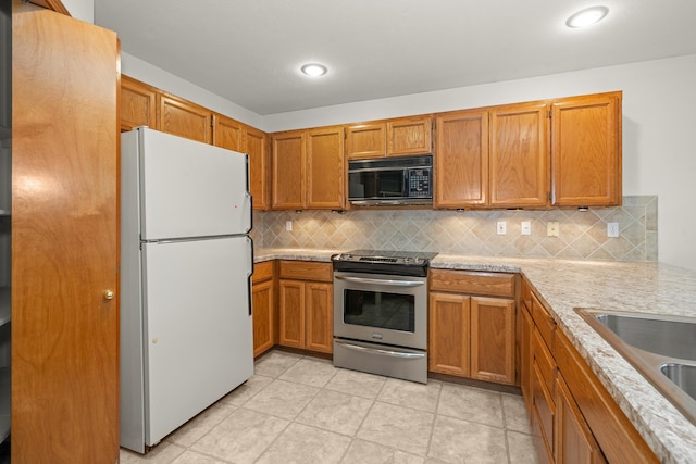 kitchen featuring black microwave, light countertops, freestanding refrigerator, tasteful backsplash, and stainless steel range with electric stovetop