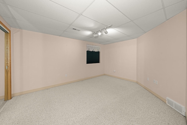 below grade area with baseboards, a drop ceiling, visible vents, and track lighting