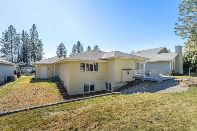 rear view of property with a shingled roof, a deck, and a lawn