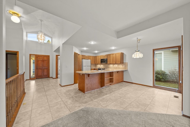 kitchen featuring stainless steel microwave, backsplash, brown cabinetry, freestanding refrigerator, and a peninsula