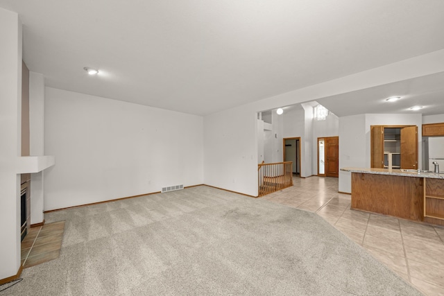 unfurnished living room featuring light tile patterned floors, light colored carpet, a fireplace, visible vents, and baseboards