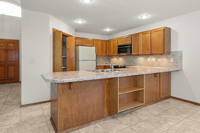 kitchen featuring black microwave, a peninsula, a sink, light countertops, and freestanding refrigerator