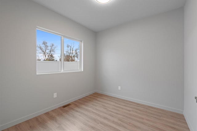 empty room with light wood-style floors, visible vents, and baseboards