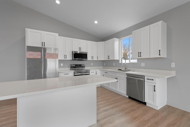 kitchen with stainless steel appliances, vaulted ceiling, a sink, and light wood finished floors