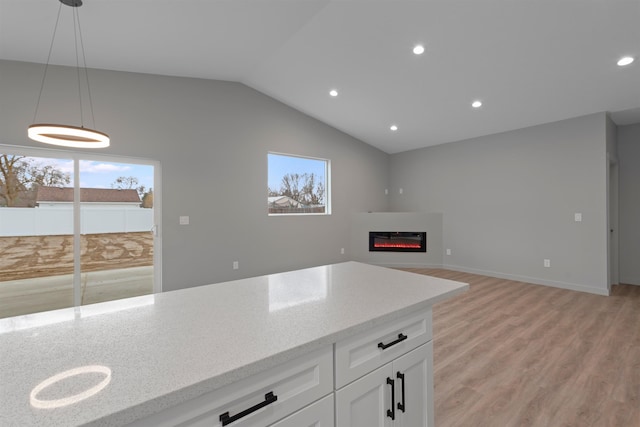 kitchen with light wood-style floors, vaulted ceiling, light stone countertops, a glass covered fireplace, and decorative light fixtures