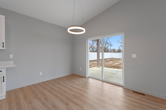 unfurnished dining area featuring lofted ceiling, light wood finished floors, baseboards, and visible vents