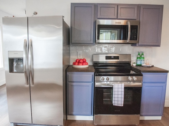 kitchen with dark wood finished floors, decorative backsplash, dark countertops, stainless steel appliances, and gray cabinetry