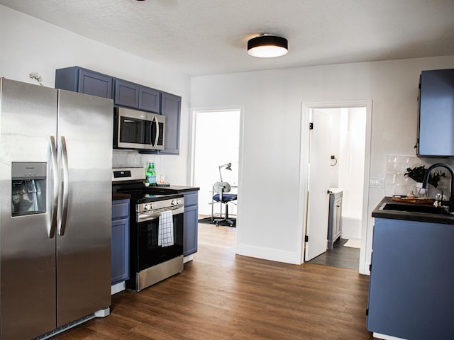 kitchen featuring dark wood-style flooring, stainless steel appliances, decorative backsplash, a sink, and blue cabinets