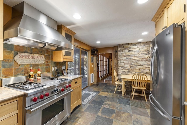 kitchen featuring appliances with stainless steel finishes, light countertops, wall chimney range hood, and tasteful backsplash