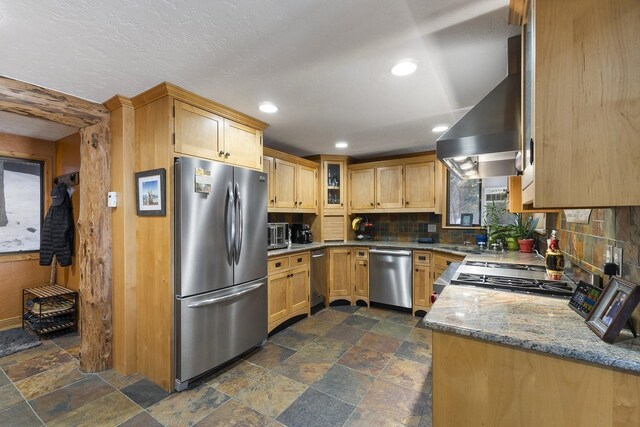 kitchen with light stone counters, stainless steel appliances, wall chimney range hood, tasteful backsplash, and stone tile flooring