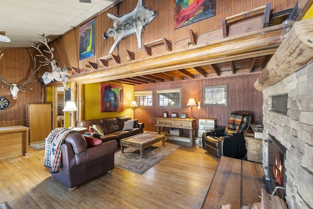 living area featuring a stone fireplace, wood walls, wood-type flooring, and a towering ceiling