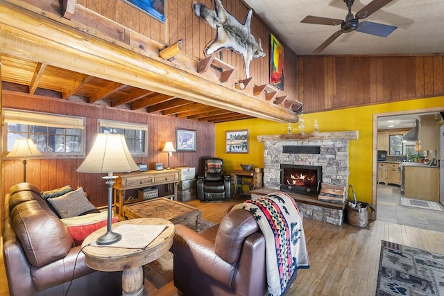 living area with ceiling fan, a fireplace, wooden walls, and hardwood / wood-style flooring