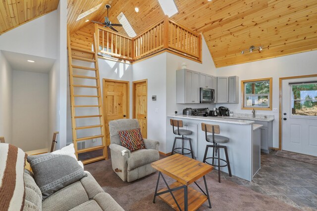 living room with a skylight, baseboards, a ceiling fan, wood ceiling, and dark carpet