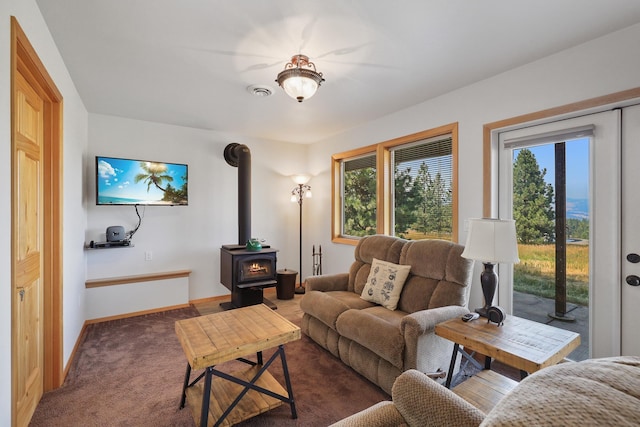 carpeted living room featuring a wood stove, baseboards, visible vents, and a wealth of natural light