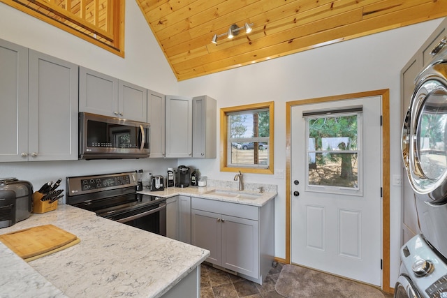6152 Winding River Way, Fruitland, WA 99129 - kitchen featuring appliances with stainless steel finishes, stacked washer and clothes dryer, gray cabinetry, vaulted ceiling, and light stone countertops