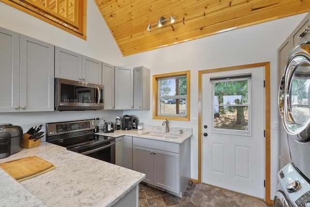 kitchen with appliances with stainless steel finishes, stacked washer and dryer, a sink, and gray cabinetry