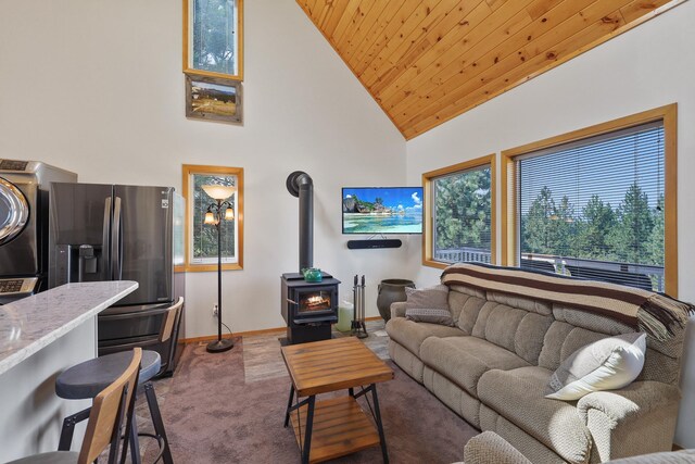 carpeted living area featuring high vaulted ceiling, wood ceiling, baseboards, stacked washer / drying machine, and a wood stove