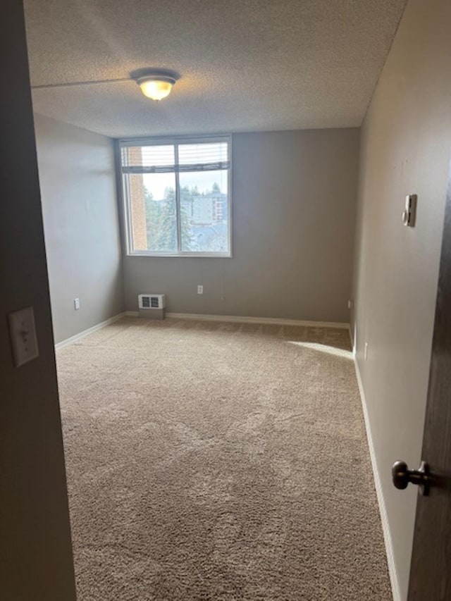 empty room with visible vents, a textured ceiling, baseboards, and carpet