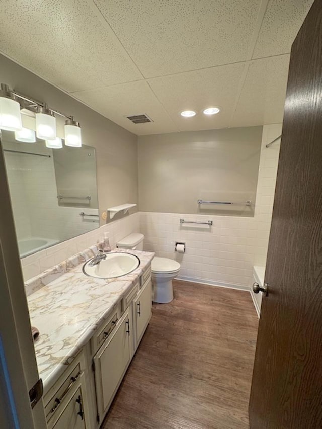 bathroom featuring visible vents, toilet, wood finished floors, tile walls, and vanity