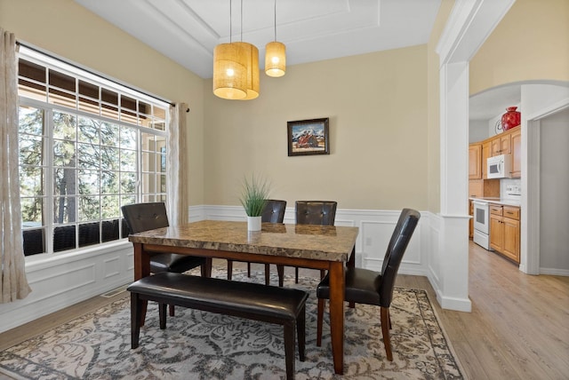 dining room with arched walkways, a raised ceiling, wainscoting, light wood-style flooring, and a decorative wall