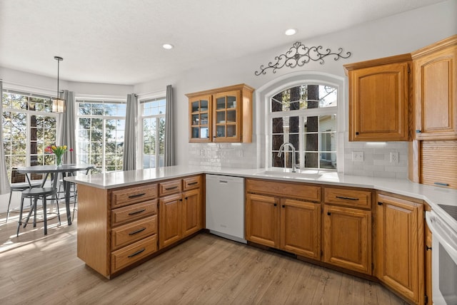 kitchen with a peninsula, a sink, light countertops, dishwasher, and light wood finished floors